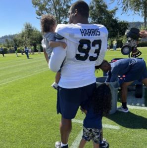 Shelby Harris of the Seahawks with his children. His son has FPIES. Shelby is in his uniform and they are standing on a field.