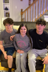 Nicole and her brothers sit on the couch and smile at the camera. 