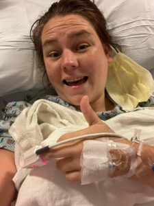 Kyla in the hospital for her Gleich syndrome. She smiles at the camera and gives it a thumbs up