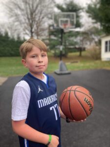 Griffin, who has hemophilia A, stands in his jersey on the basketball court. He holds a basketball in his left hand.