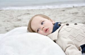 Rowan, who passed away from Krabbe disease, on the beach. He is propped up on a white pillow.