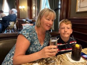 Jo and Oscar, who both have NF2, sit at the dinner table at a restaurant. Jo is wearing a blue dress and smiling at the camera. Oscar has strawberry blonde hair and is partially smiling