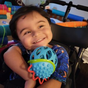 Anthony, who has CASK gene disorder, holds a toy and smiles at the camera