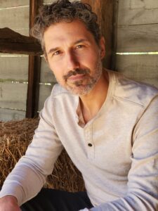 Ethan Zohn head shot. Ethan, who talks about cannabis rescheduling after his CD20+ Hodgkin's lymphoma diagnosis, smiles at the camera. He has a slight beard and mustache and wears a white shirt.