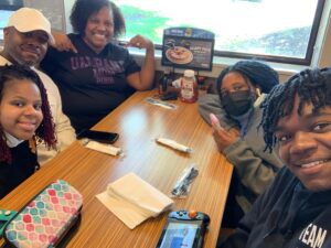 The Thorington family sits around a table. Some smile at the camera and others are wearing a mask. Ronda's daughter has MCTD.